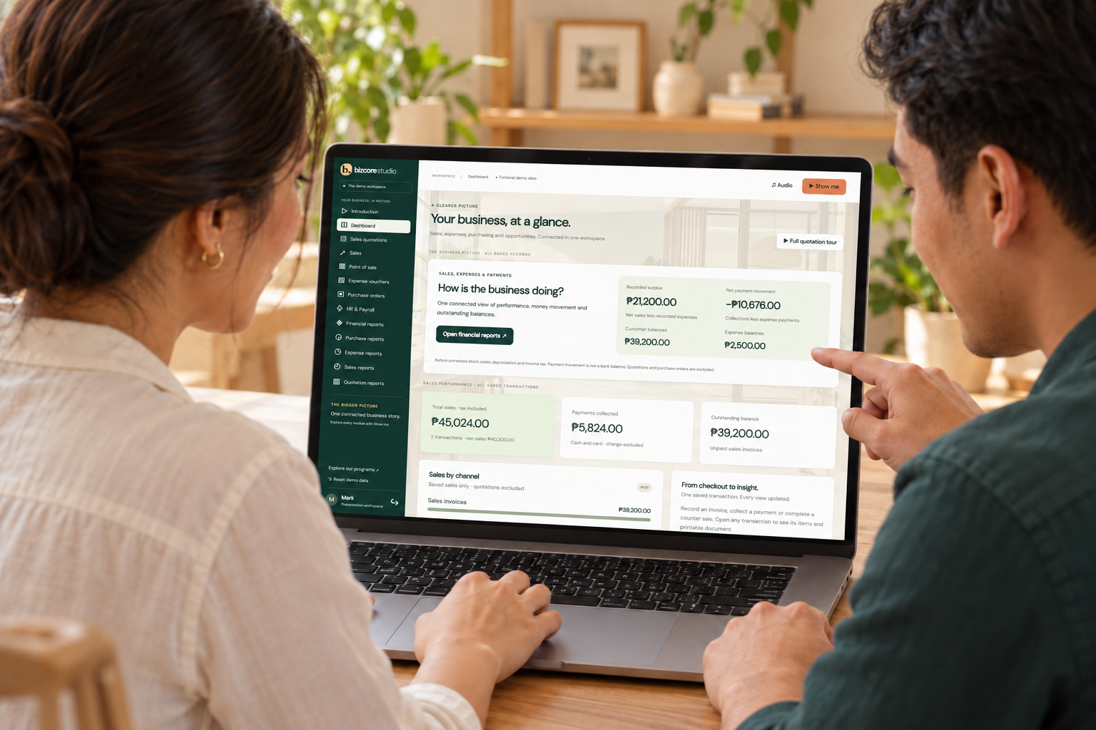 AI-generated illustration of a presenter and business owner viewing the real BizCore Studio dashboard from the same side of a laptop, with upright unsupported heads